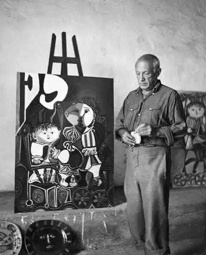 Pablo Picasso standing beside one of his paintings in his studio
