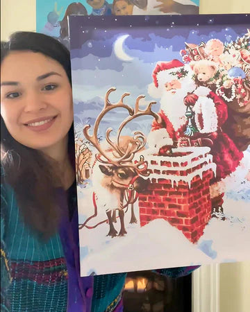 Woman holding a Christmas canvas with Santa Claus and reindeer on a snowy roof.