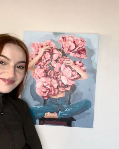 Woman standing next to a painting of pink flowers and hands
