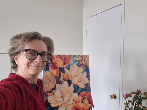 Woman with glasses standing next to a colorful floral painting in a room.