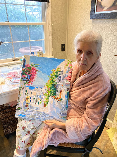 Woman holding a painting of a scenic landscape in a home setting