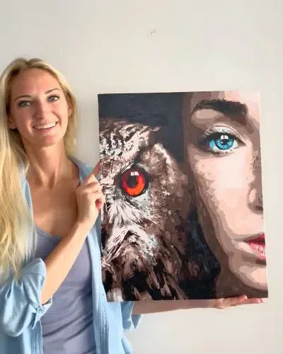 Woman holding a painting of a woman's face and an owl with a red eye.