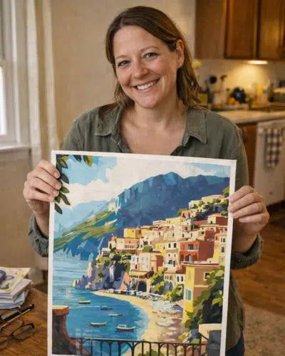 Woman holding a colorful painting of a coastal scene with buildings and mountains.