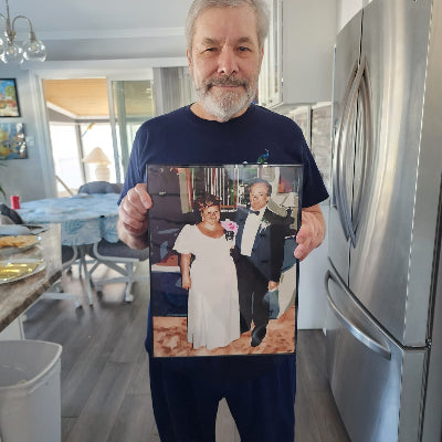 Man holding a framed custom painting of a couple in a kitchen.