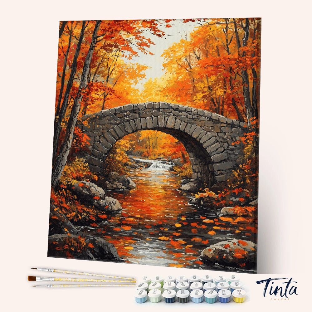 Angled display of the Autumn’s Quiet Crossing paint by numbers kit showing a rustic stone bridge over a glowing autumn creek by Tinta Canvas