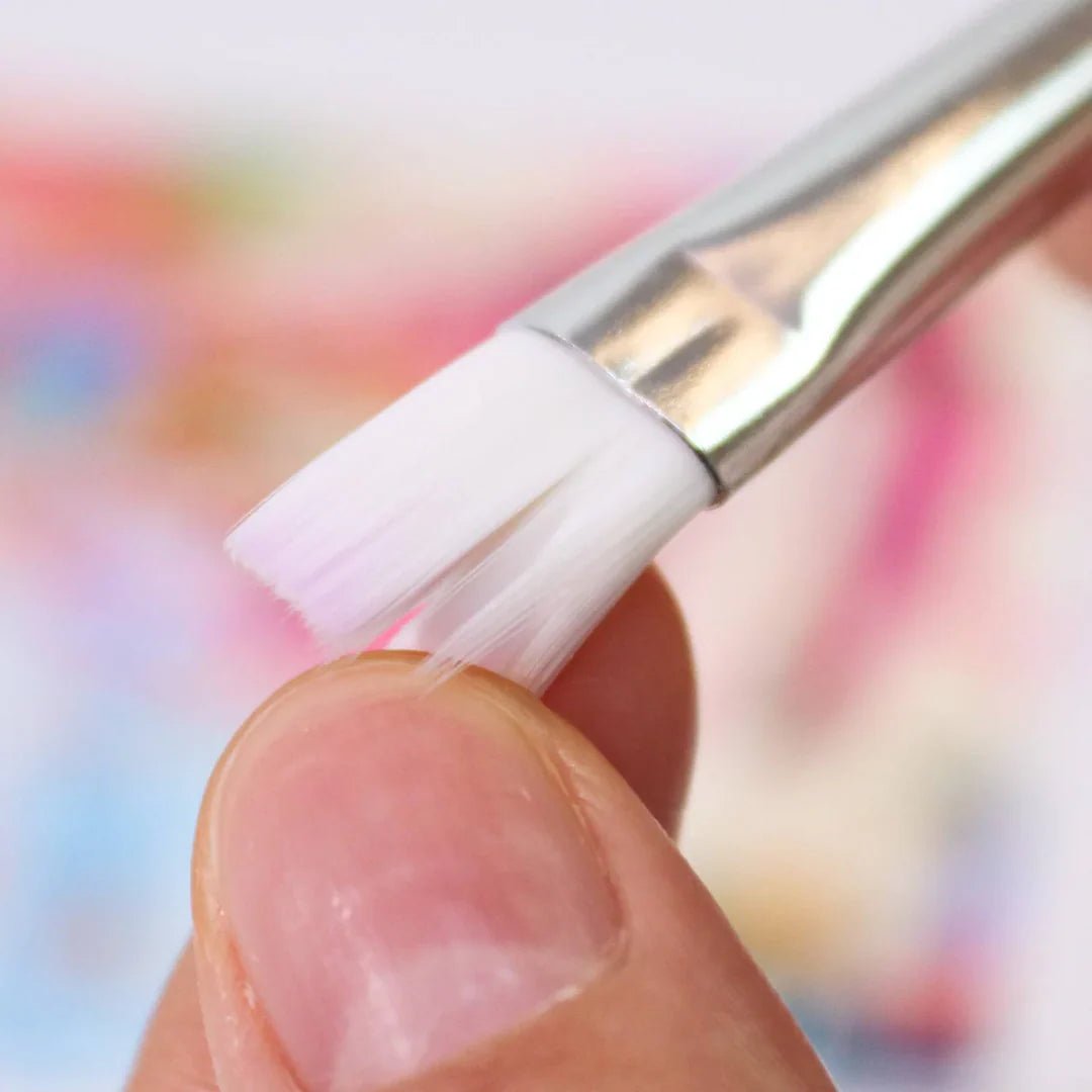 Close-up of a hand holding a makeup brush with a blurred multicolored background