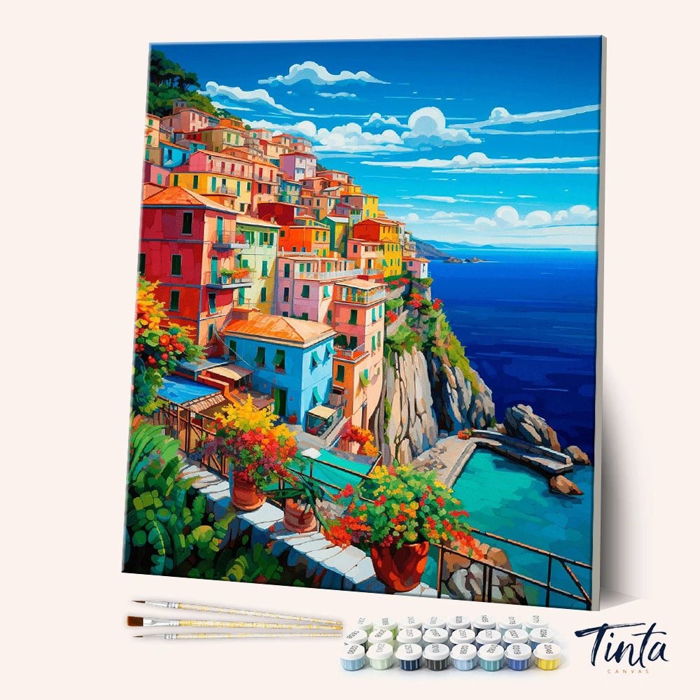Angled display of the Italian Coast paint by numbers kit showing colorful seaside village canvas with brushes and paint pots by Tinta Canvas
