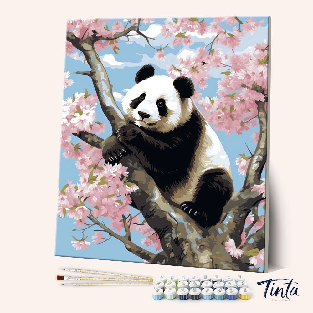 Angled display of the Panda in Bloom paint by numbers kit showing a panda resting among pink cherry blossoms by Tinta Canvas