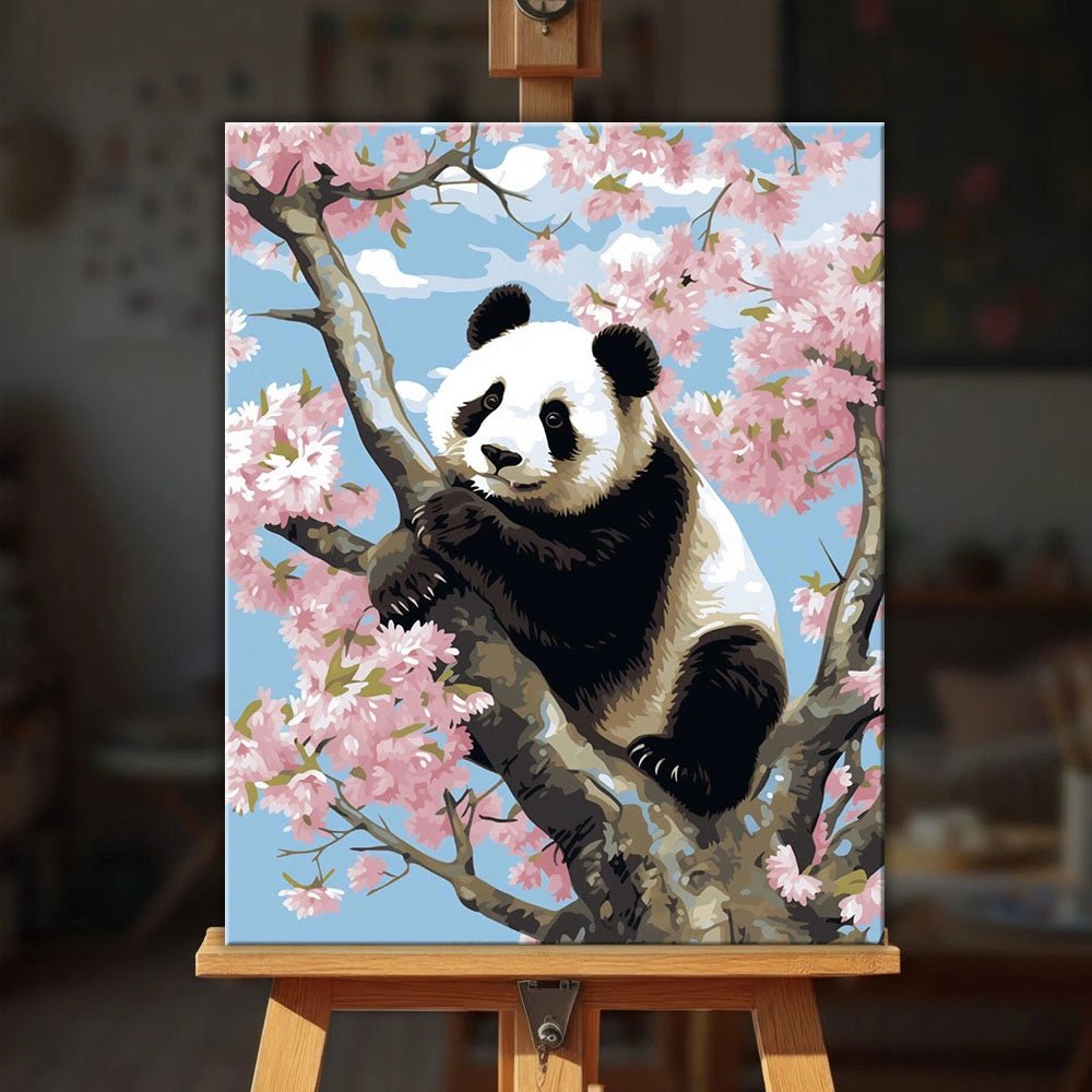 Panda in Bloom paint by numbers kit displayed on an easel showing a panda perched on a branch surrounded by pink flowers by Tinta Canvas
