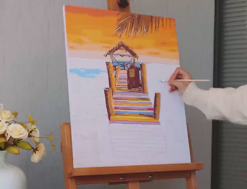 Artist painting a beach boardwalk scene using a Tinta Canvas paint by numbers kit