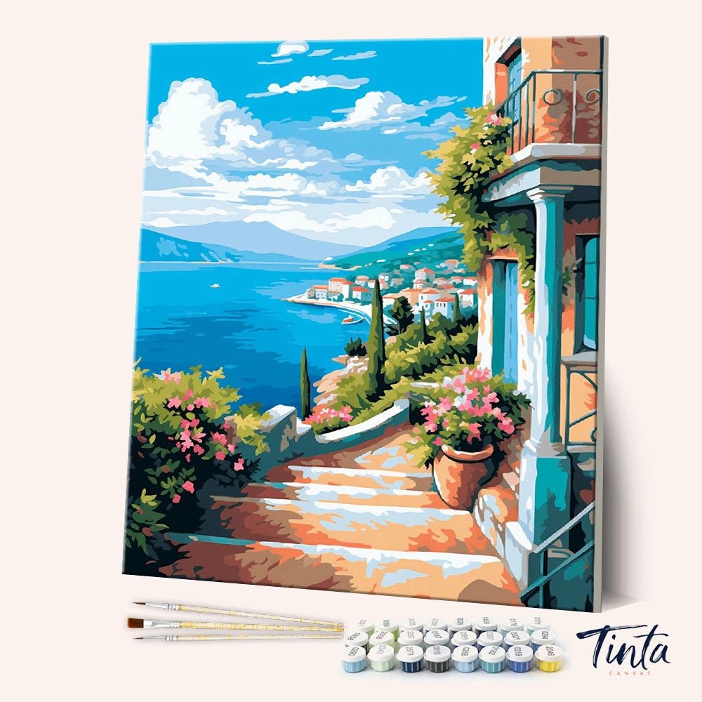 Angled display of the Sea View Terrace paint by numbers kit showing coastal terrace canvas with brushes and paint pots by Tinta Canvas