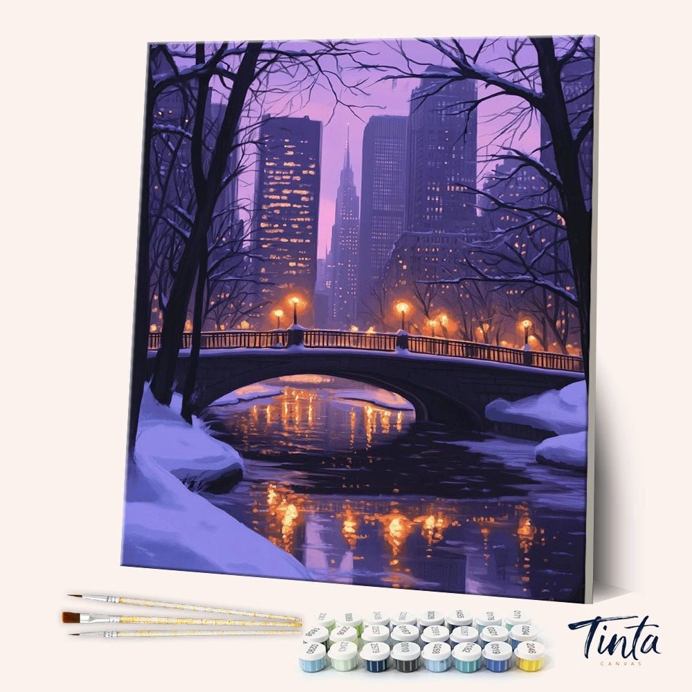 Winter Walks paint by numbers kit angled view showing snowy bridge with glowing lights and city skyline at night