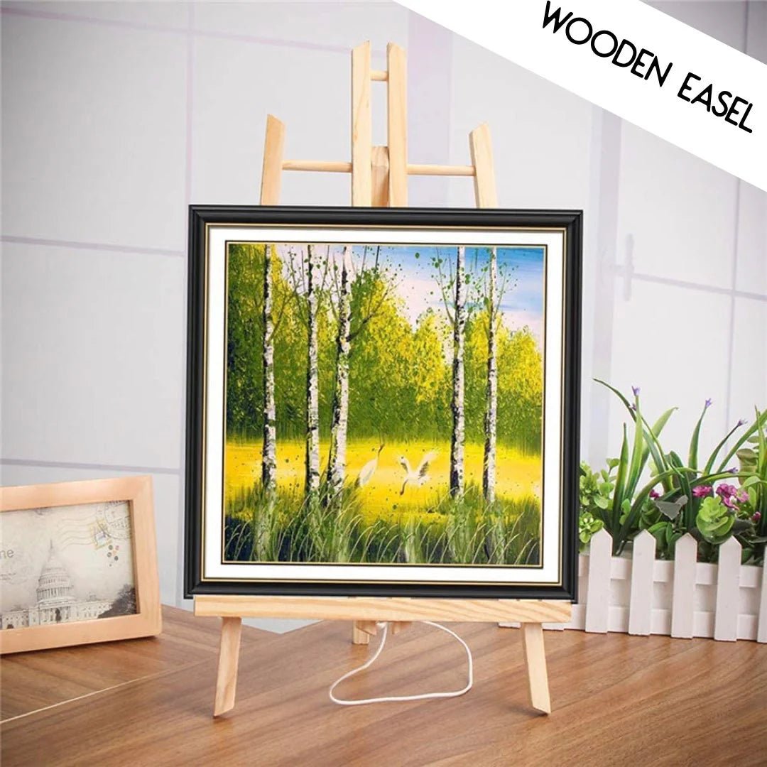 Framed painting of a forest scene on a wooden easel with a white wall background.