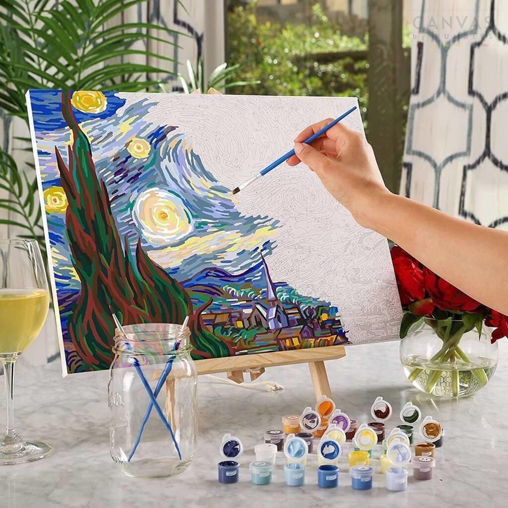 Person painting a stylized version of 'The Starry Night' with art supplies on a table.